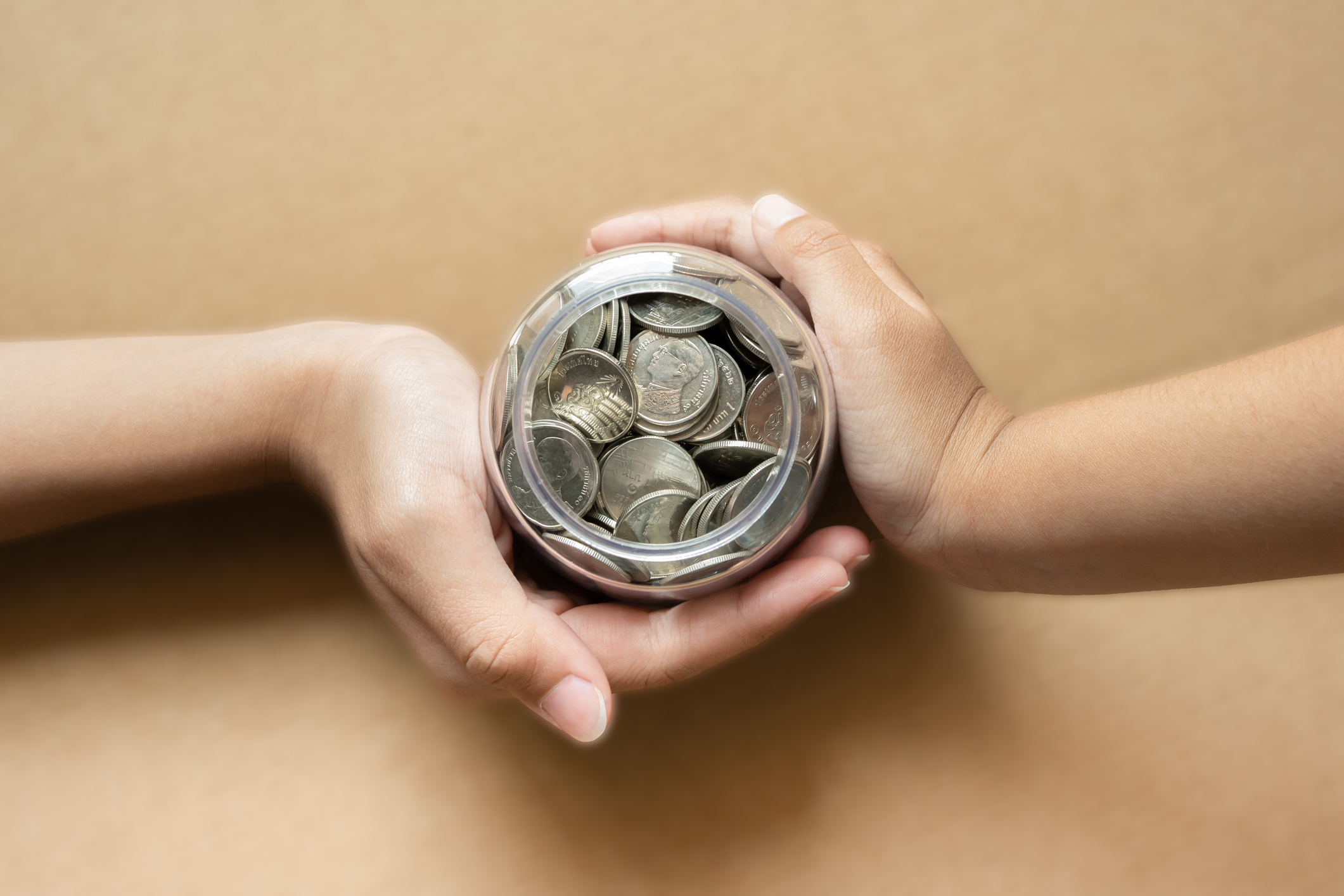 Kid hands holding coins in a jar together as saving concept for family or education. Saving concept using kid hands holding coins.