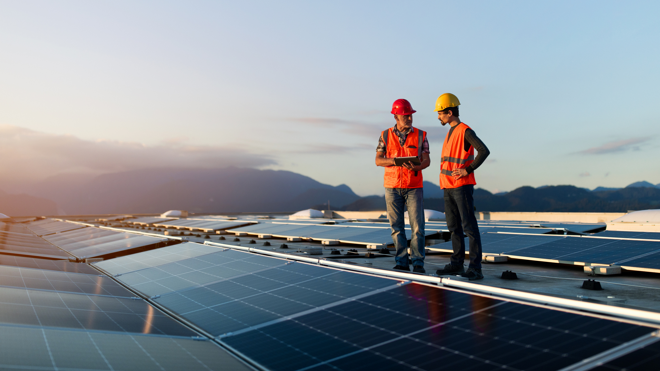 Technicians in reflective vests checking solar power plant installed on building roof